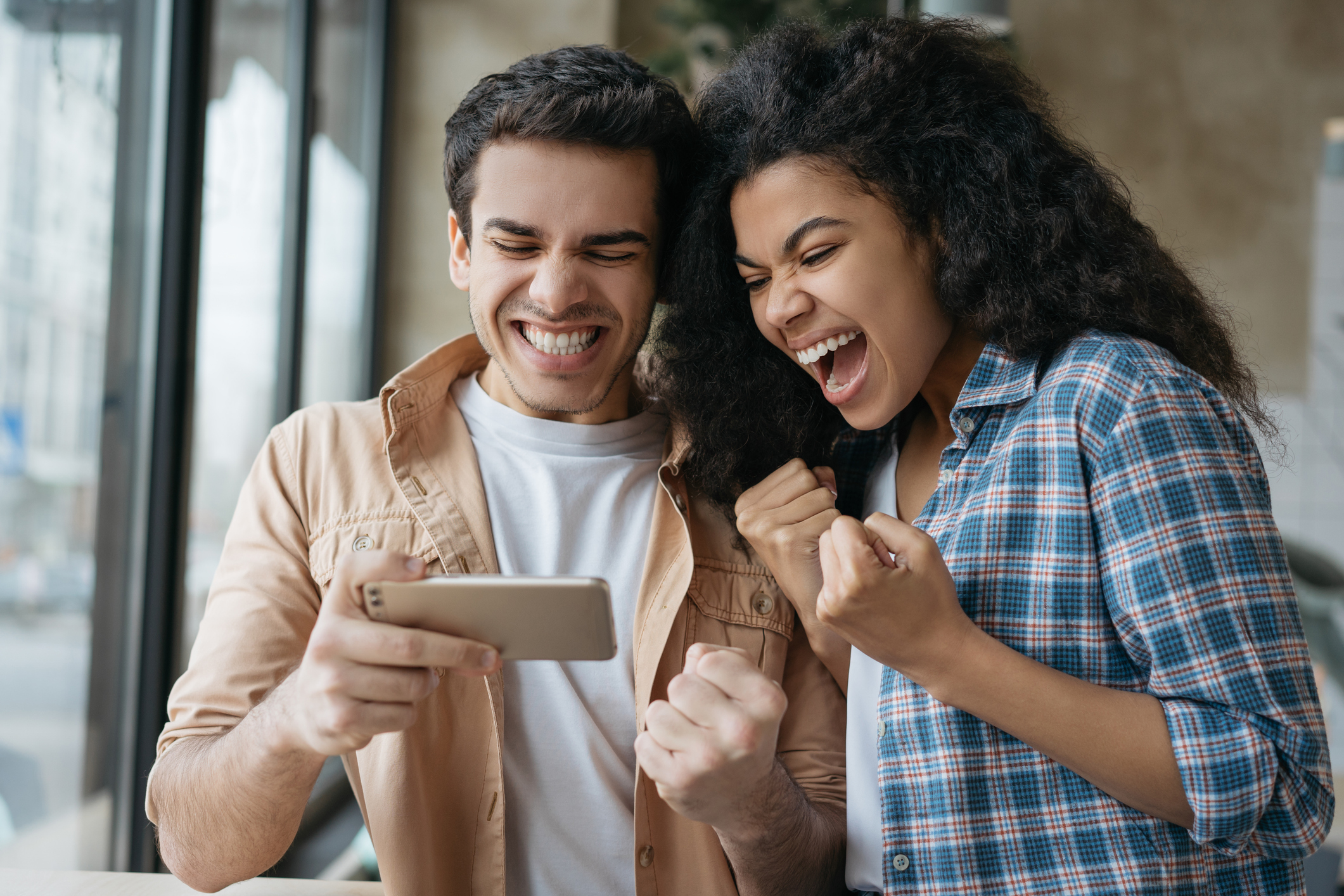 Excited friends using smart phone, playing video games. Happy emotional couple celebration success. Portrait of overjoyed online lottery winners looking at digital screen. Sport betting concept